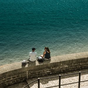 Couple sitting on a sunlit sea wall on Gun Cliff Walk, Lyme Regis 29_08_21