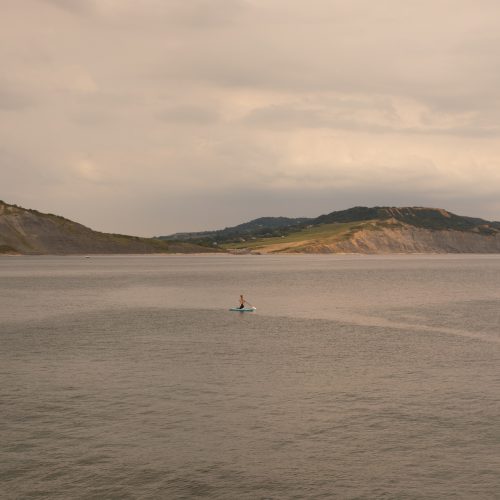 Distant paddle boarder in the bay with the coast beyond from Gun Cliff Walk Lyme Regis 01_08_24