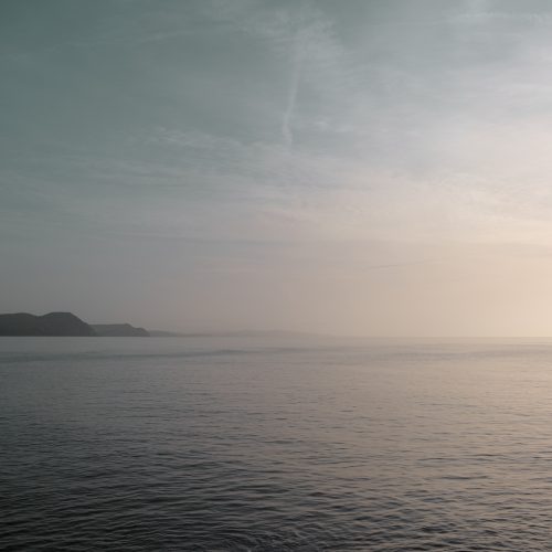Hazy morning sunlight over the sea with the coast beyond from Front Beach Lyme Regis 01_02_24 edit
