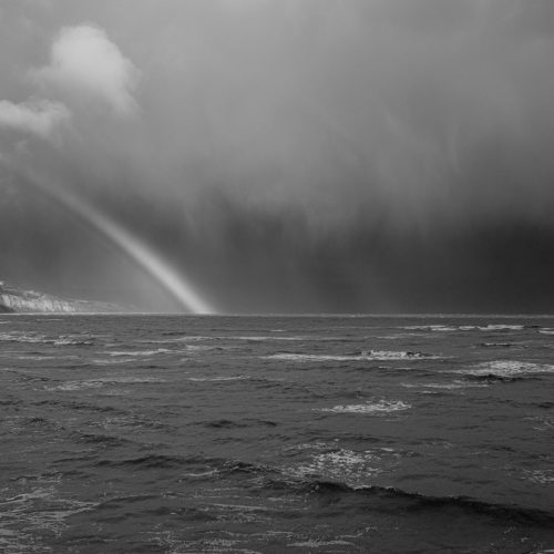 Rainbow in sunlight and a stormy sky over the coast from Church Cliff Walk Lyme Regis ACROS R 27_03_24 1 mono