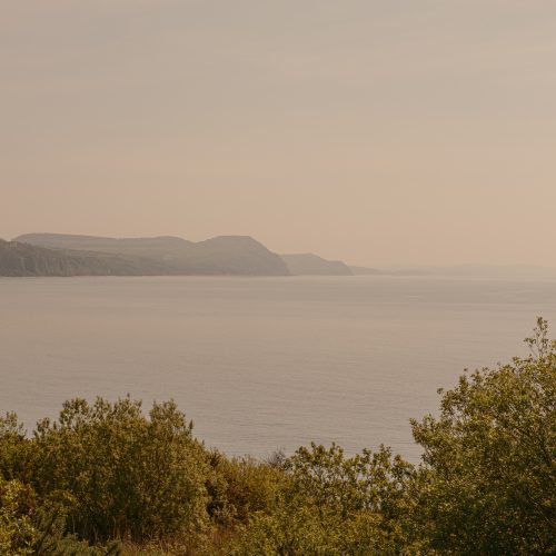 Sunlit view over the coast and sea from the Charmouth Road car park path to Church Cliff Walk Lyme Regis 09_05_24