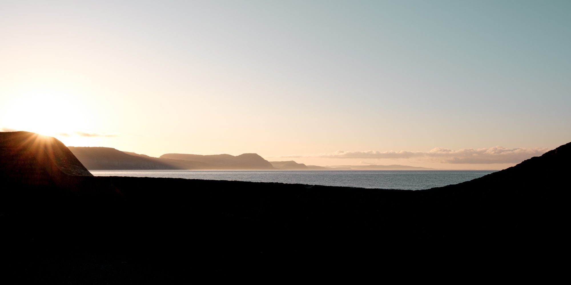 Sunrise over the coast and sea through the dip in the sea wall on Gun Cliff Walk Lyme Regis 04_05_24 1 pano
