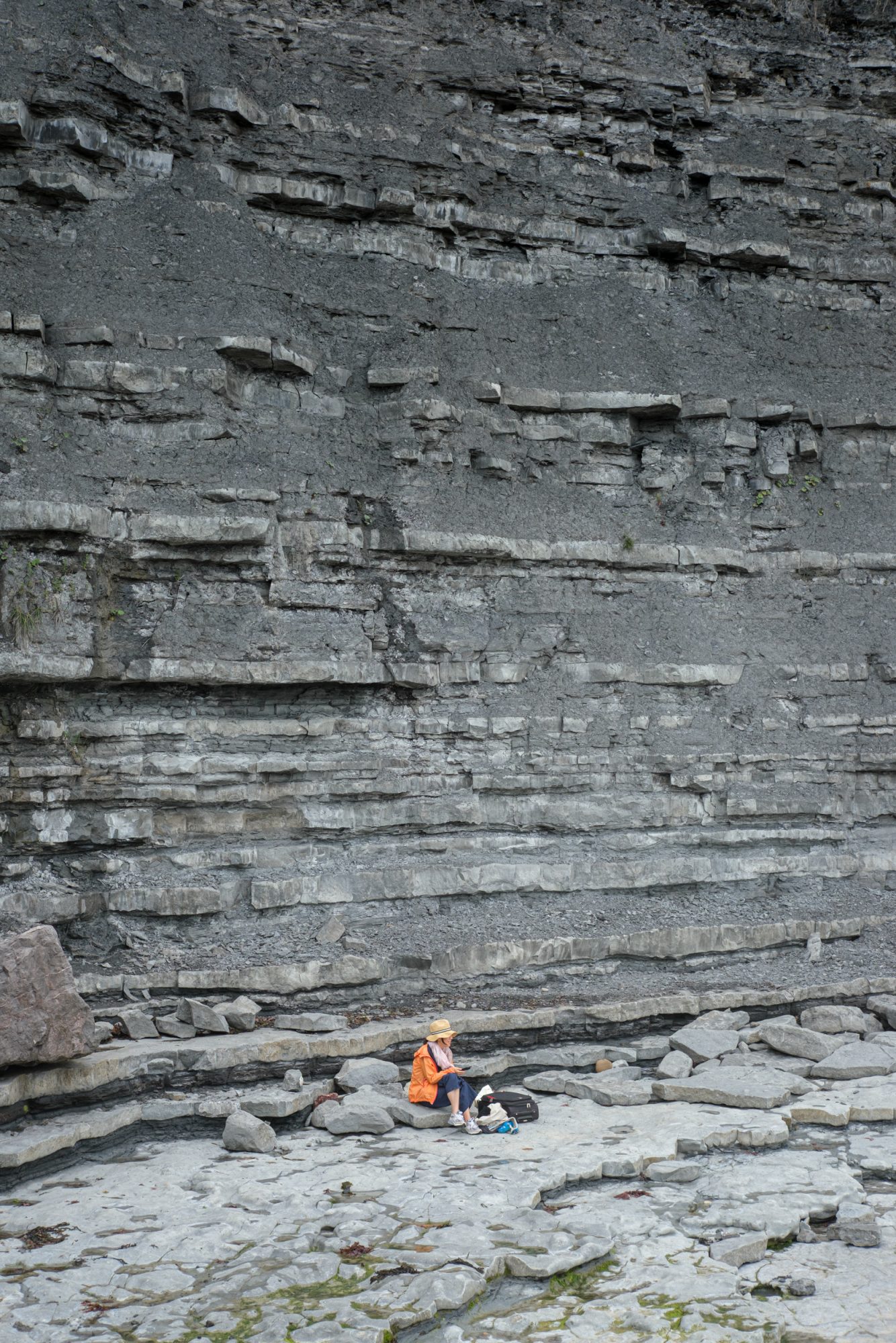Woman on her phone sitting on fallen rock at the foot of East Cliff Lyme Regis 23_07_24 2