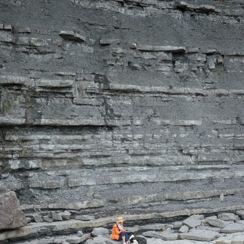 Woman on her phone sitting on fallen rock at the foot of East Cliff Lyme Regis 23_07_24 2